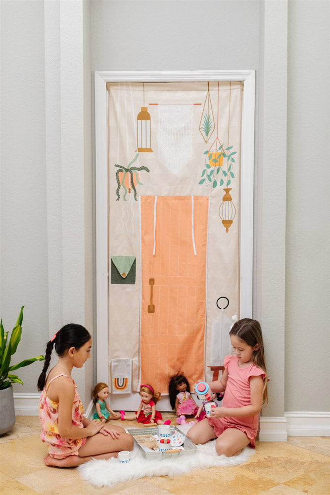 Two little girls having a tea party with a Boho style playhouse that hangs in the doorway. Sophisticated playroom design ideas