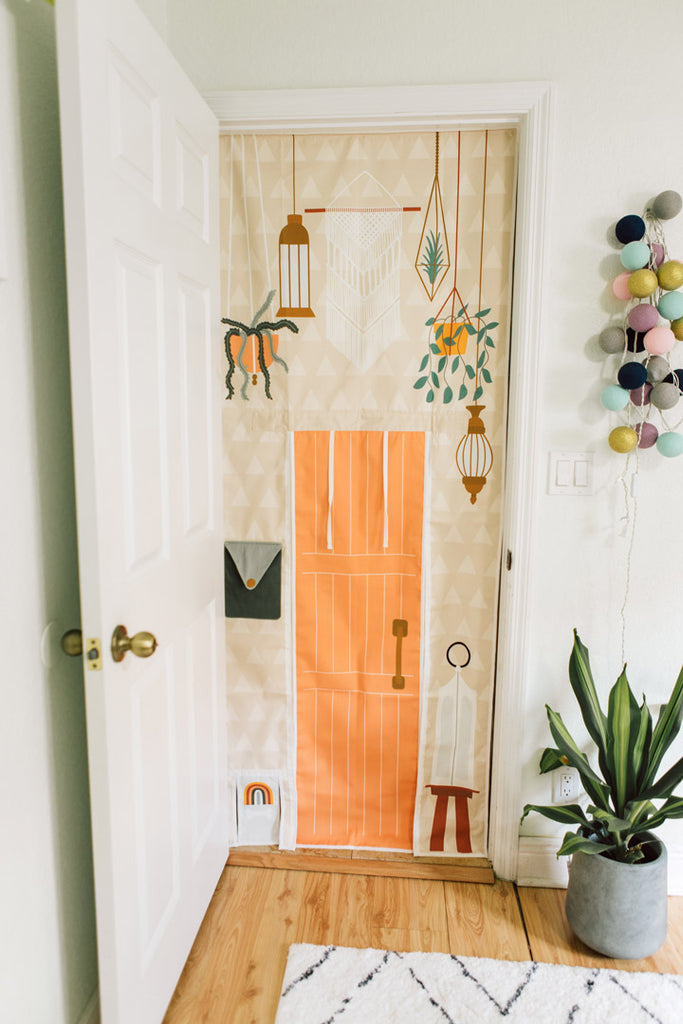 Boho style doorway playhouse with roll up doors, doggie door, and mailbox for imaginary play. Kids playroom interior design ideas