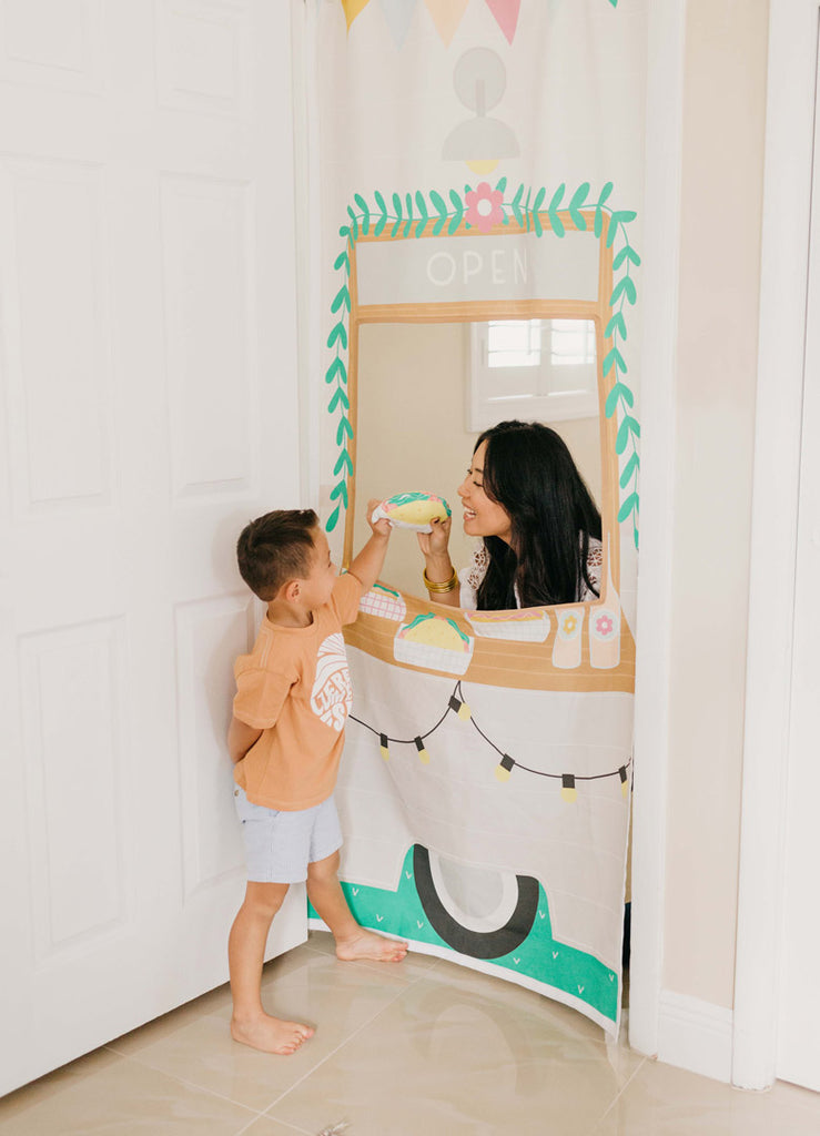 Mom giving toddler boy a pretend play taco while playing with a Pretend play Food Truck storefront that hangs in the doorway. Creative kid's playroom design ideas